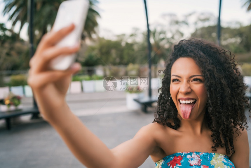 年轻美国拉丁女人在街上用手机户外拍自的肖像图片