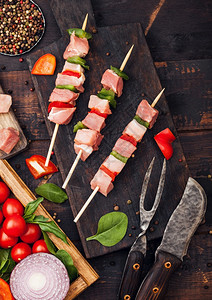 生猪肉烤和辣椒在切板上新鲜蔬菜在木本底叉子和刀盐辣椒与生菜和樱桃番茄图片