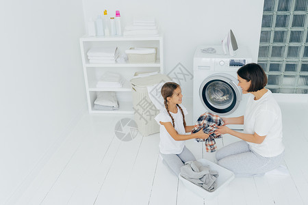 衣着脏服的洗机在宽敞的洗衣房里摆姿势在家做务互相快乐地看着对方图片