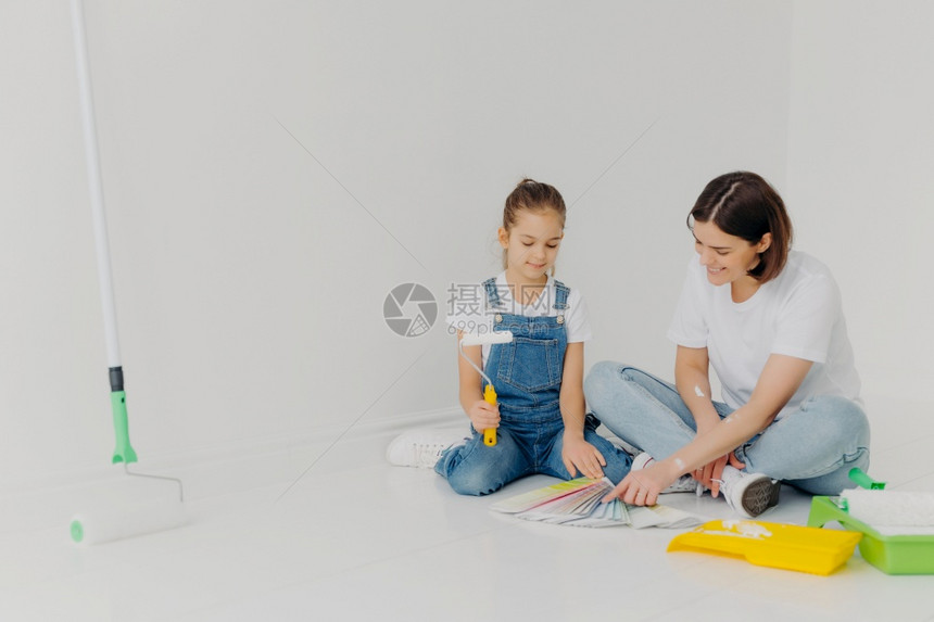 女孩和母亲坐在地板上仔细看彩色调板选择画室的最佳颜色使用建筑工具在宽敞的白色房间里摆姿势图片