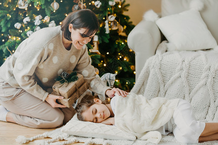 美丽的有爱心母亲准备这个盒子给睡在圣诞树旁背景图片
