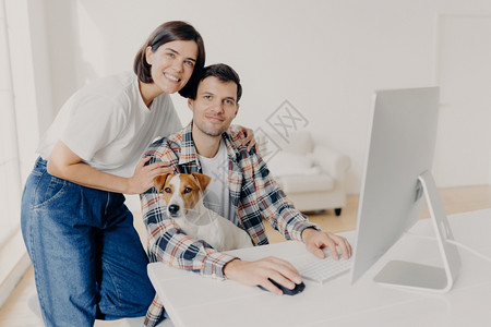 工作辛巴狗幸福的丈夫和妻子在电脑键盘和冲浪信息附近摆姿在家庭气氛中与狗一起工作在空间中摆姿与无线互联网连接背景
