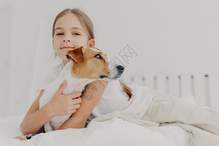 小女孩拥抱狗呆在床上图片