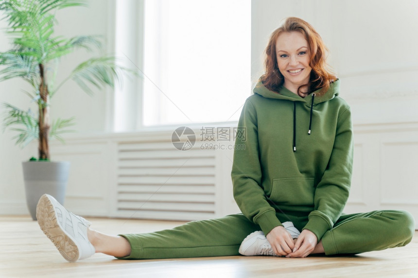 有运动机的女表现出良好的灵活身材瘦弱腿伸展运动穿绿色服白鞋坐在地板上更喜欢健康的生活方式图片
