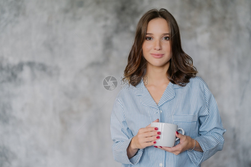 穿夜衣的有吸引力女子用咖啡或茶白色杯子或咖啡茶用白色杯子喝早酒以模糊的背景在室内装饰并有供广告或宣传内容的复制空间图片