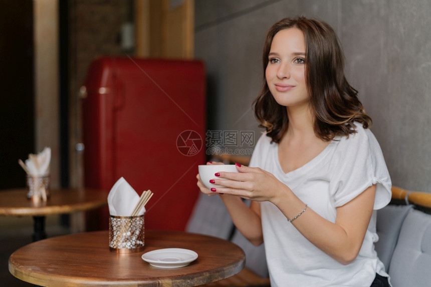 穿着白衬衫面容快乐喝芳香咖啡在餐厅闲暇时间坐在圆木桌有深思熟虑的表达方式到远处图片