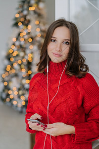 穿着红色毛衣使用手机和耳享受家庭气氛在过圣诞节图片