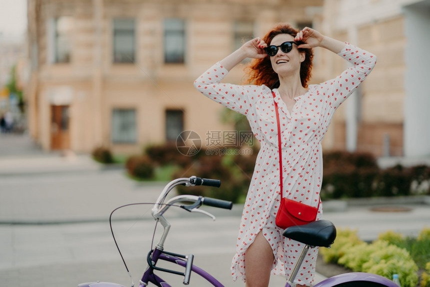 城市中快乐的无照顾妇女周期近身骑自行车握着窗帘穿白衣服享受夏季时间和节假日专心于城市背景模糊的空白复制间图片