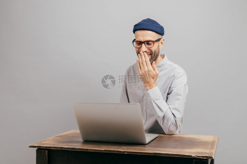 成年男博客与追随者聊天发送反馈享受自由时间微笑阅读有趣的新闻用棕榈覆盖嘴穿正规衣服隔着灰色背景图片