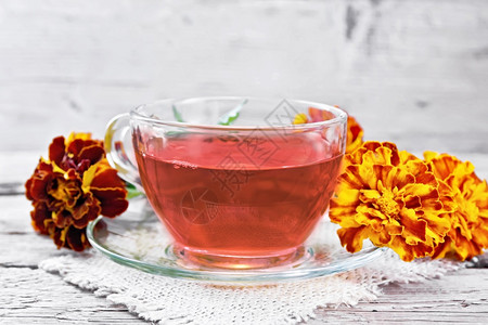 玻璃杯和茶碟里盛着的马格德草药茶餐巾纸上装满麻布和木板上鲜花的图片