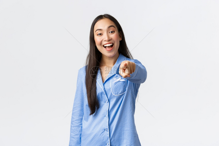 欢乐的美丽穿着蓝睡衣的亚洲女孩指着镜头笑微挑选或择你做决定自信站在白色背景之上欢乐的美丽亚洲女孩指着相机笑站在白色背景之上图片