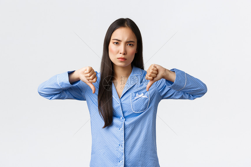 穿着蓝色睡衣的失望迷年轻女表示不喜欢现出低缩的怀疑判断产品或皮肤护理化妆品差对质量和白背景不满意失望的穿蓝色睡衣年轻女表示不喜欢图片