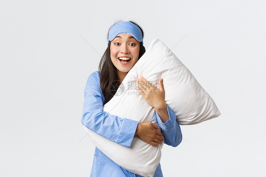穿着蓝睡衣和面具的美丽笑的亚洲女孩拥抱软舒适的枕头图片