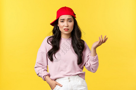人们的情绪生活方式闲暇和美丽概念持怀疑态度的没有印象穿红色帽子韩国女孩举起手来说这样的话感到不关心和粗感到不关觉黄色背景人们的情背景图片