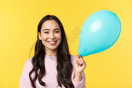 人们的情感生活方式休闲和美丽概念可爱笑的亚洲女孩拿着蓝色的气球拿着蓝色的气球以庆祝大型活动站在黄色背景上背景图片