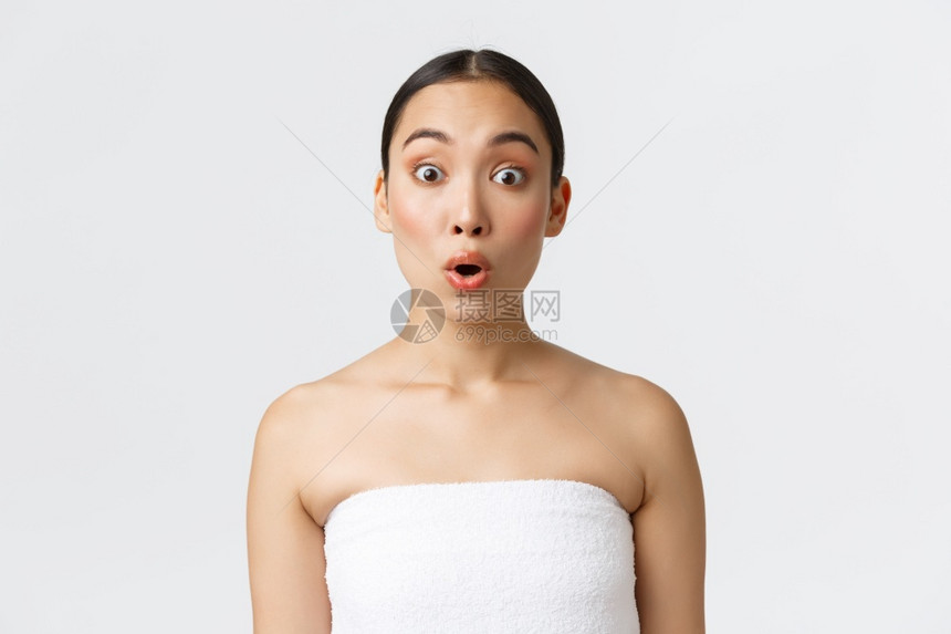 令人印象深刻和好奇的亚洲女孩听到有趣的宣传提议站在白色背景的毛巾上发表温泉沙龙的广告美容产品皮肤护理用白色背景令人印象深刻和好奇图片