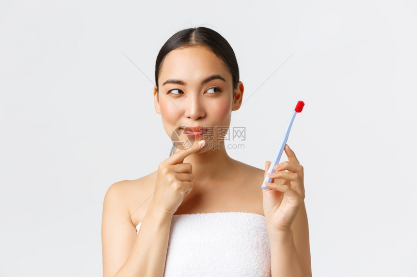 穿着浴巾拿牙刷和思想有法刷牙时白背景美貌个人照顾卫生概念思想图片