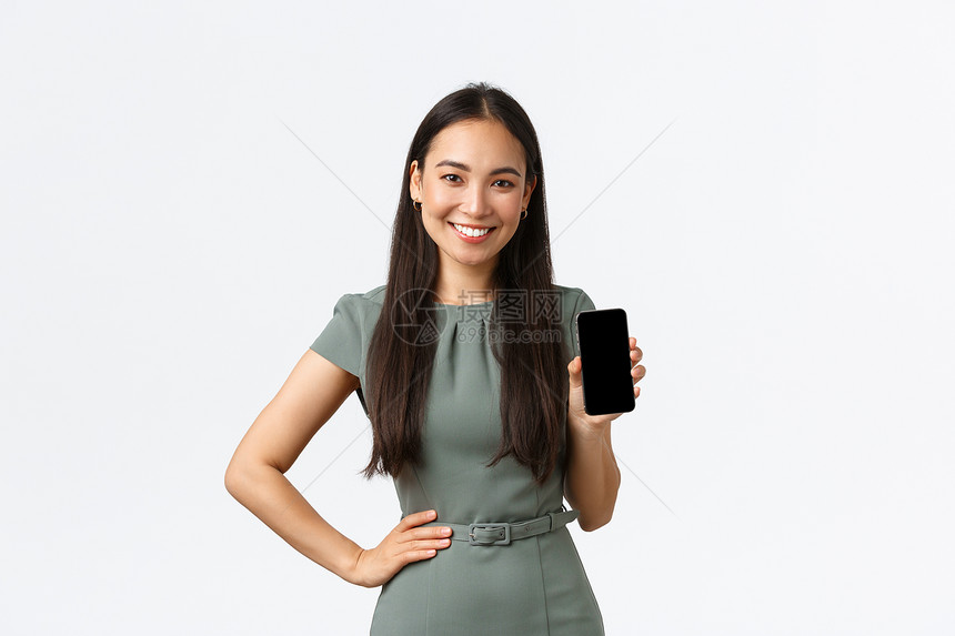 小型商业主女企家概念微笑着美丽的亚洲女穿着智能手机屏幕推荐移动应用程序显示中的应用程序站立的白色背景小商业主微笑着漂亮的亚洲女穿图片