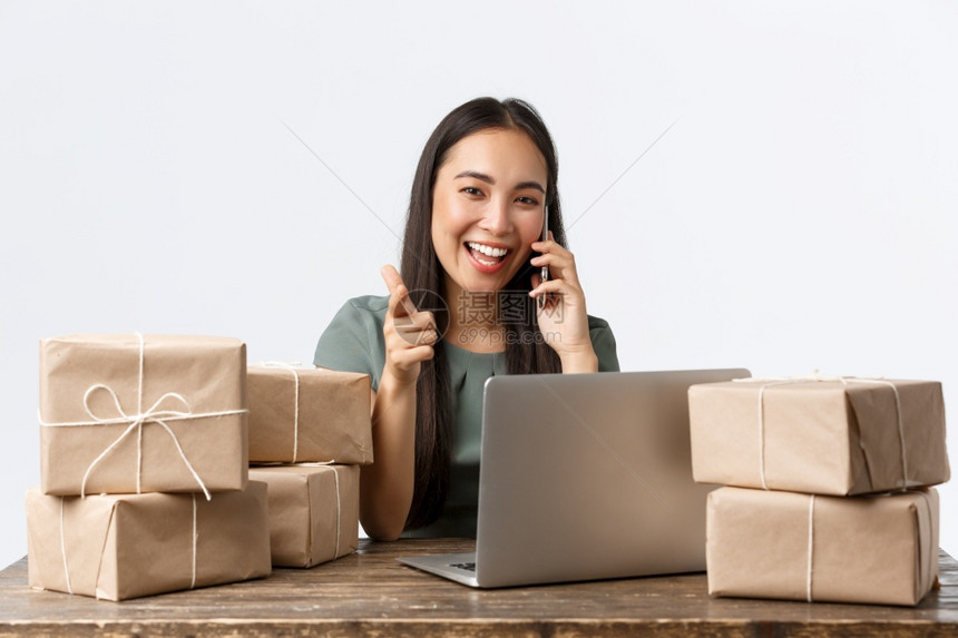 小企业所有者创和电子商务概念微笑作为女商人在线店经理指着相机回答顾客电话用笔记本包装船的箱小业主运包箱图片
