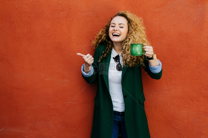 穿着夹绿色咖啡的克举起她拇指表示对喝的满意图片