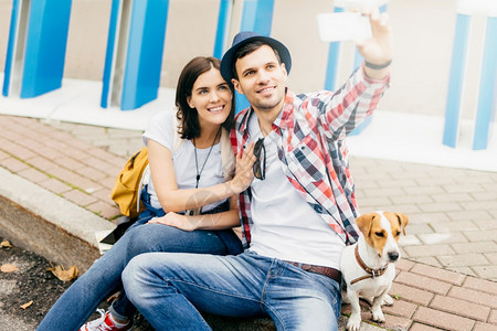 与女友和狗坐在一起的英俊青年男子拿着智能手机制作自拍购物后放松图片