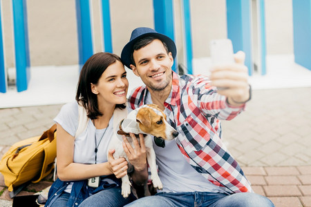 带着狗坐在人行道上用手机自拍脸上笑着愉快同时欢乐地共度空闲时光图片