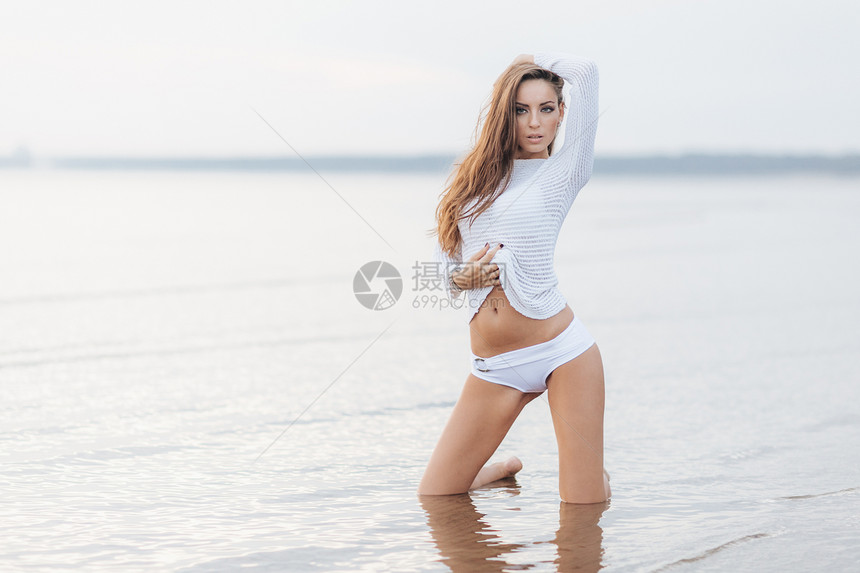 穿着白色比基尼完美的身材跪在沙滩上与海或背景相比热辣的美女在暑假期间户外放松图片
