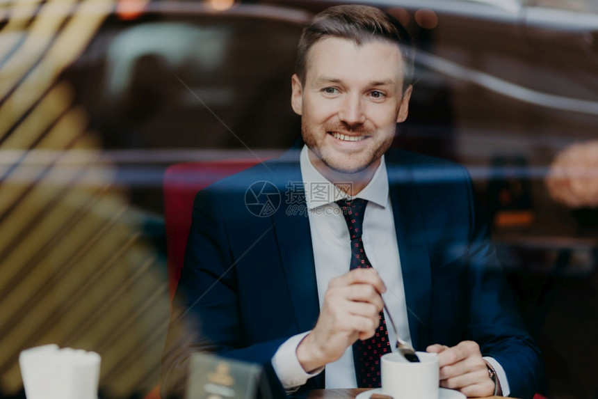 穿着正式衣服的快乐商人横向镜头喝芳香的热饮坐在自助餐厅时看着窗户图片