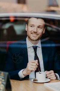 男企业家在正规服装喝咖啡快乐的表达抛开在咖啡馆闲暇时间在近窗处摆姿势图片