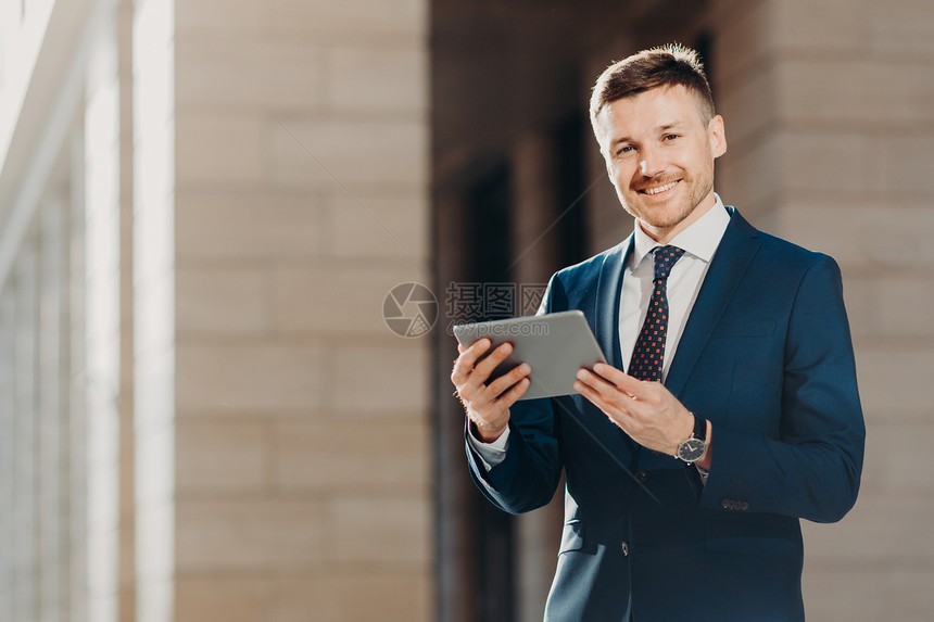 快乐的男企业家穿正式的黑西装拥有现代平板电脑检查网络中金融新闻与无线互联网连接编写商业会议的财务报告图片