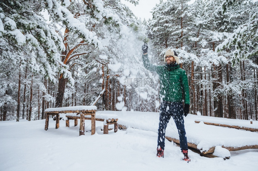 在户外拍摄身着温暖衣服的英俊长胡子男玩得开心如空投雪在冬季森林度假表示积极图片