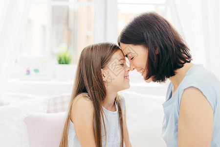 亲切的年轻母和她小女儿吻鼻子享受在一起白色背景和卧室内装扮愉快地微笑背景图片