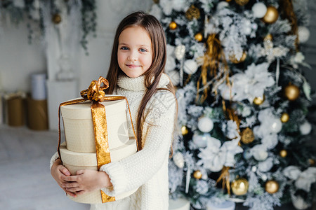 室内可爱的小女婴穿着温暖的编织衣服拿着巨大的包礼物图片