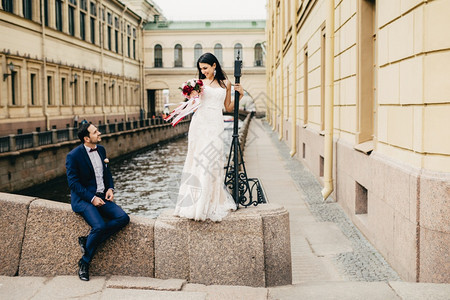 英俊的新郎坐在桥上看着他美丽的新娘她站起来向致意享受在一起有难忘的时刻在一起浪漫的人和婚礼概念背景图片