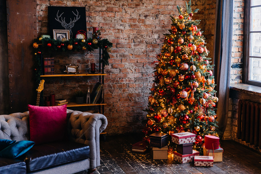 有砖墙的舒适公寓和光亮装饰的圣诞树和下面的一堆礼物图片