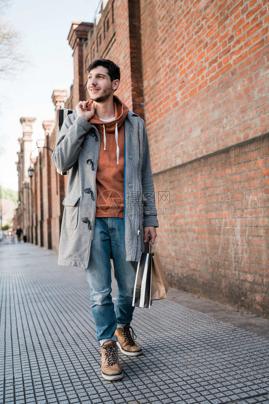 年轻英俊男子在街上散步时拿着购物袋的肖像城市商店概念图片