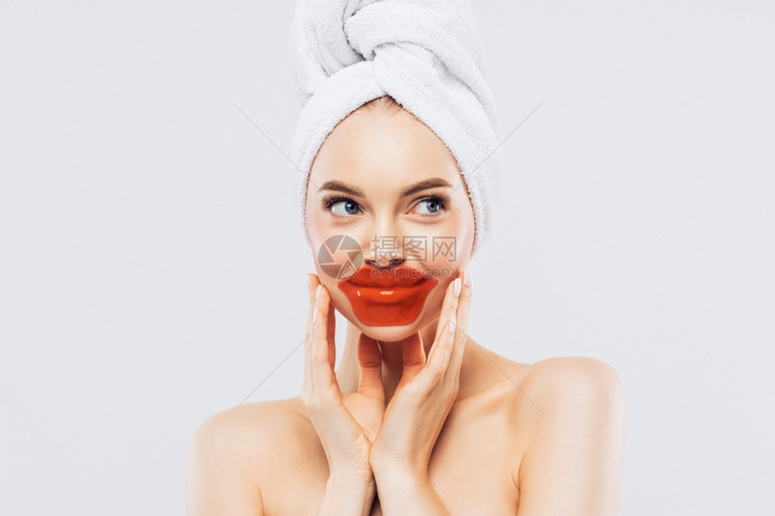室内放松的妇女有新鲜健康的皮肤在嘴唇上佩戴斑纹头白毛巾在温泉沙龙接受面部治疗图片