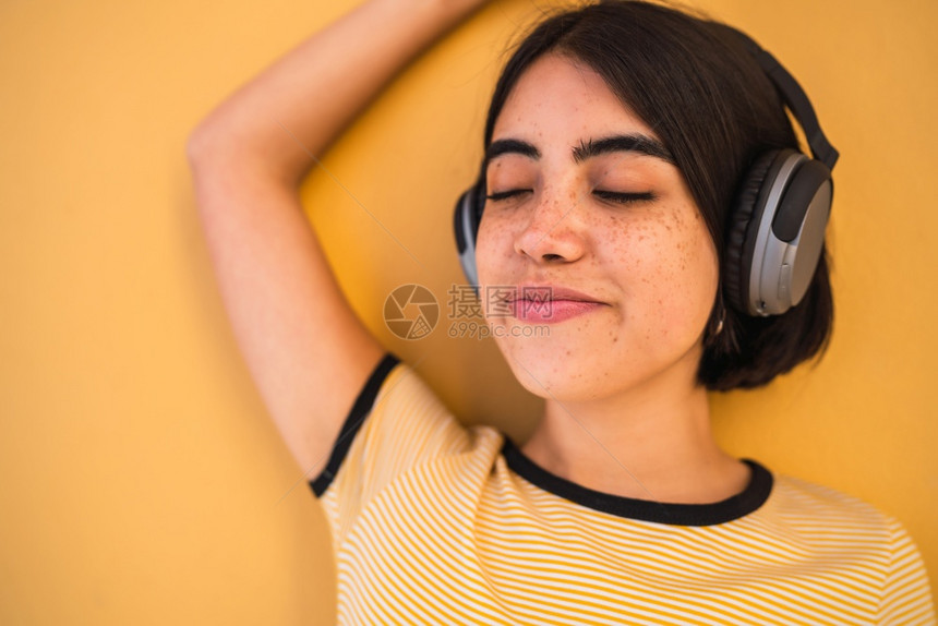 在黄色背景下用耳机收听音乐的年轻拉丁妇女肖像城市概念图片