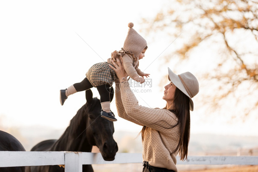 在秋天阳光明媚的日子里年轻母亲和小女婴在马匹旁边图片