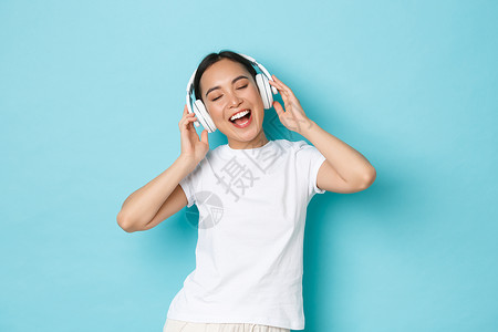 歌唱比赛素材购物金钱和融概念欢快的亚洲女孩穿白色散装t恤唱卡拉ok播放音乐应用程序听无线耳机音乐并享受完美的声音购物播放音乐应用听无线耳机音背景