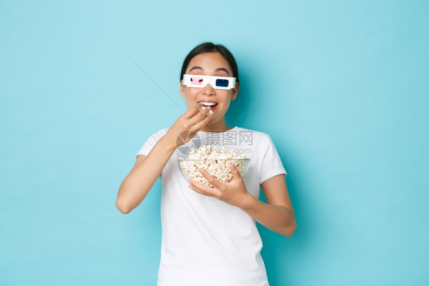 生活闲暇和情绪概念年轻兴奋的亚洲女孩观看最喜爱电影首映穿着3d眼镜吃爆米花时用兴奋的表情站立浅蓝色背景生活方式闲暇和情绪概念年轻图片