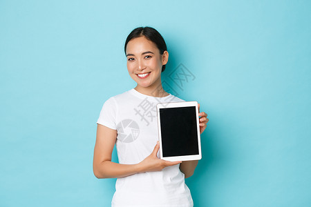 在数字平板屏幕上展示项目或广告介绍新的购物网站在浅蓝背景上站立起来笑的有吸引力亚洲女孩在数字平板屏幕上展示项目或广告在浅蓝色背景背景图片