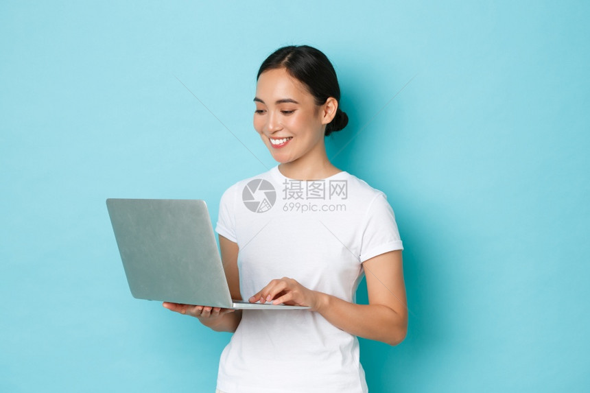 穿着白色t恤衫工作在项目上笔记本电脑屏幕上看着满意和快乐自由或browingter在浅蓝背景上线购物穿着白色t恤衫在线购物浅蓝色图片