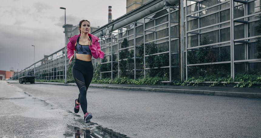 青年女运动员在工业区的雨季运行女动员在工业区行图片