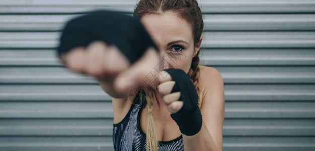 女运动员用拳击绷带看镜头和拳击关注背景的面孔女运动员看镜头和拳击图片