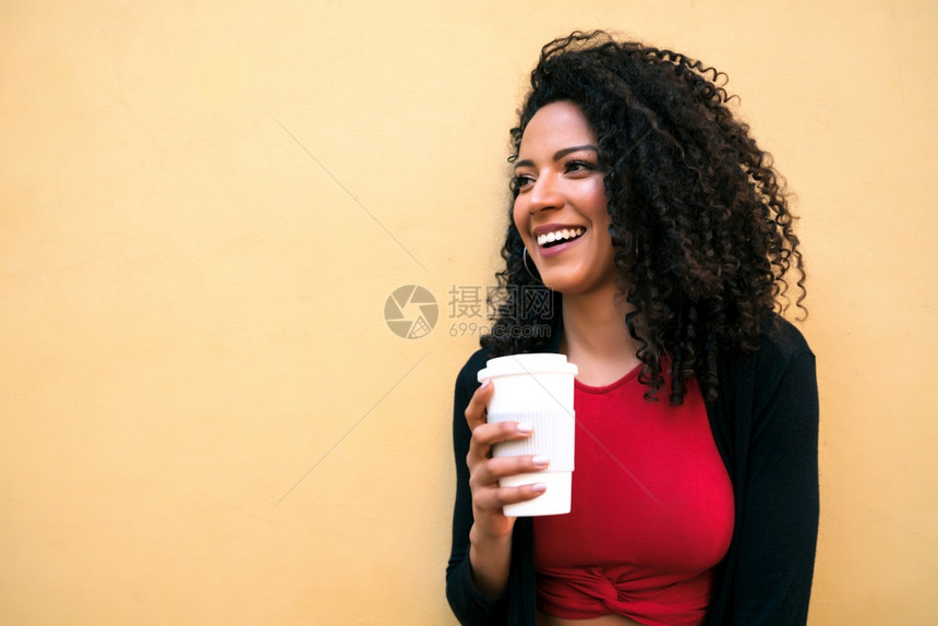 年轻美籍女在黄色背景下举杯咖啡时图片