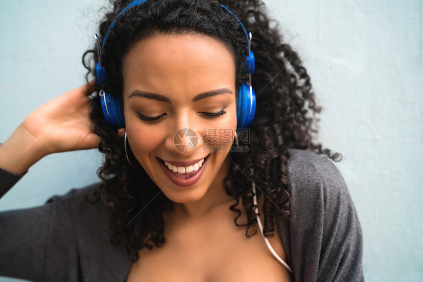 年轻fro妇女以蓝耳机享受和听音乐的肖像技术和生活方式概念图片