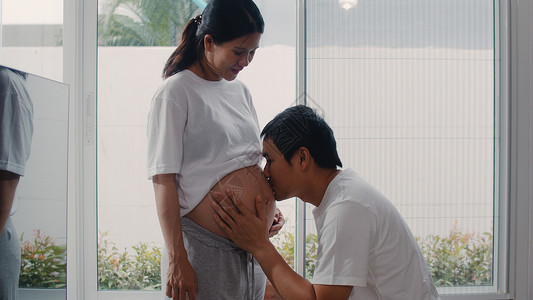 母亲和父在照顾婴儿家客厅窗户附近怀孕时开心地笑着背景图片