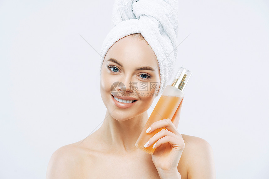 微笑积极的年轻女子拿着一大瓶香味的和鲜花照顾得体的外衣健康皮肤头上戴浴巾图片