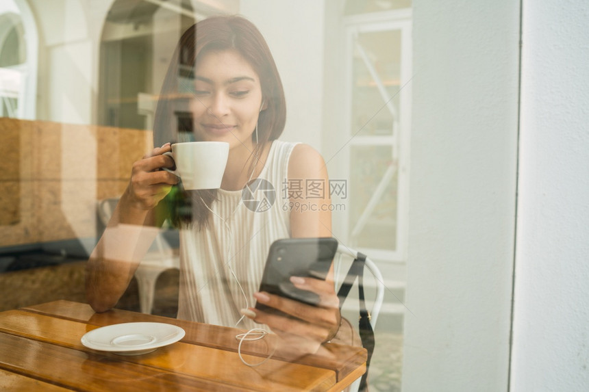 年轻拉丁女坐在咖啡店时使用手机的肖像图片